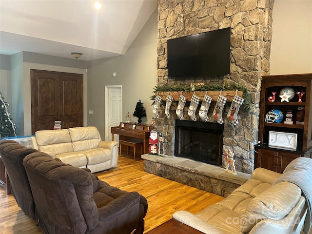 living room featuring vaulted ceiling, a stone fireplace, and light hardwood / wood-style flooring