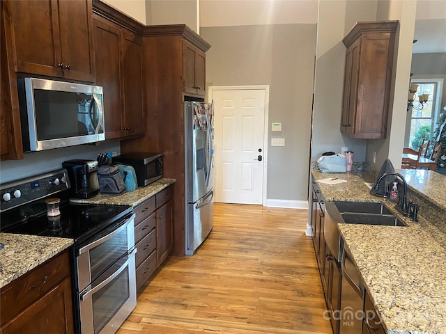 kitchen with sink, appliances with stainless steel finishes, light hardwood / wood-style floors, light stone counters, and dark brown cabinetry