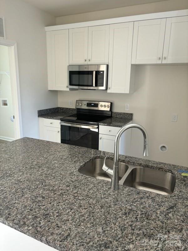 kitchen featuring appliances with stainless steel finishes, sink, white cabinetry, and dark stone countertops