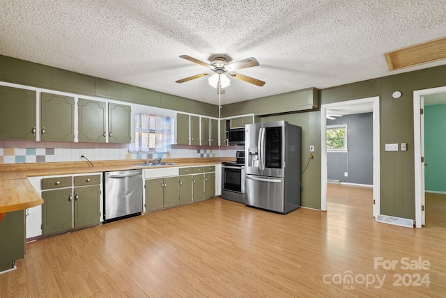 kitchen featuring sink, stainless steel appliances, backsplash, light hardwood / wood-style floors, and a textured ceiling