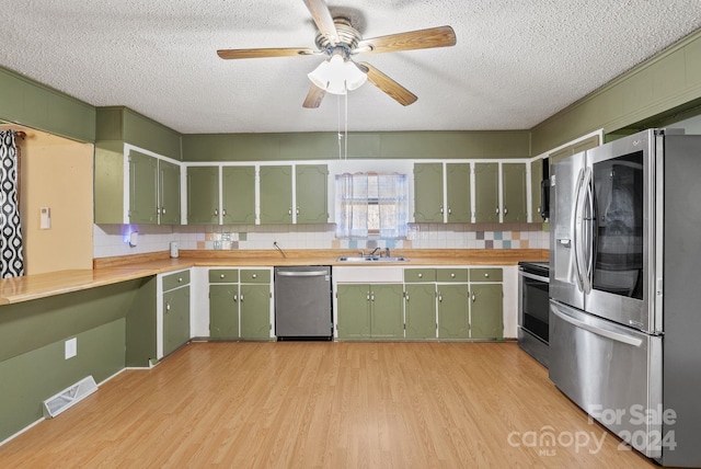 kitchen featuring sink, stainless steel appliances, light wood-type flooring, and green cabinetry