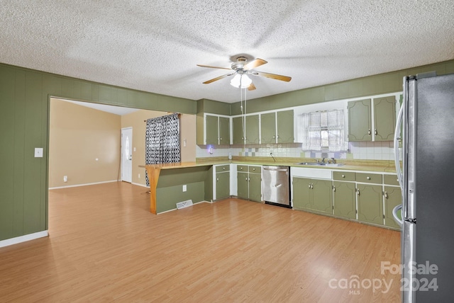 kitchen featuring green cabinetry, a textured ceiling, appliances with stainless steel finishes, tasteful backsplash, and light hardwood / wood-style floors