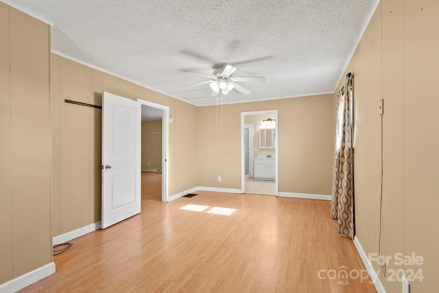 unfurnished bedroom with ceiling fan, ensuite bathroom, light hardwood / wood-style floors, a textured ceiling, and ornamental molding