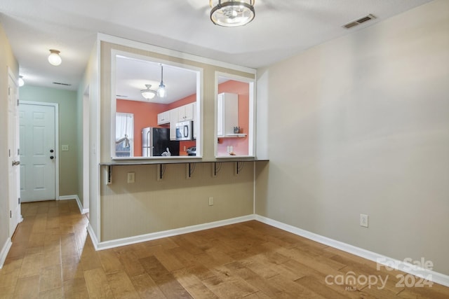 kitchen with white cabinets, a kitchen breakfast bar, appliances with stainless steel finishes, and light hardwood / wood-style flooring