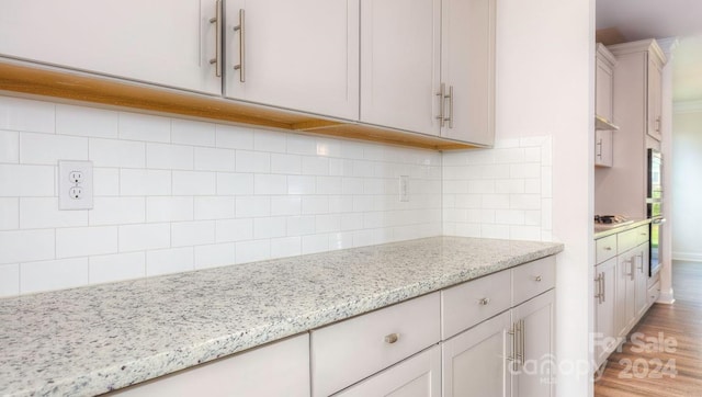 kitchen featuring decorative backsplash, light stone countertops, hardwood / wood-style floors, and stainless steel oven