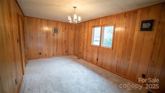 spare room with light carpet, wooden walls, and an inviting chandelier