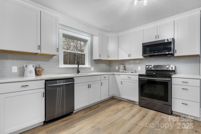 kitchen featuring stainless steel appliances, white cabinetry, sink, and light hardwood / wood-style floors