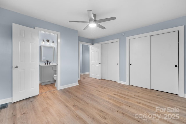 unfurnished bedroom featuring sink, connected bathroom, ceiling fan, light wood-type flooring, and two closets