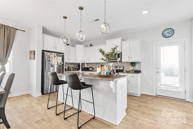 kitchen with light wood-type flooring, stainless steel appliances, stone counters, white cabinets, and an island with sink