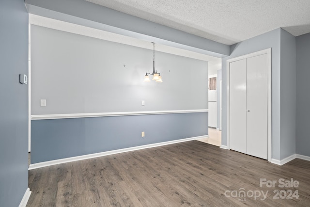 empty room featuring dark hardwood / wood-style flooring, a textured ceiling, and an inviting chandelier