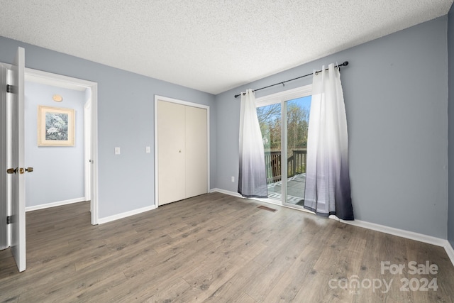 unfurnished bedroom featuring wood-type flooring, a textured ceiling, access to outside, and a closet