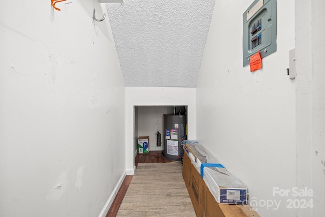 hall featuring hardwood / wood-style flooring, vaulted ceiling, a textured ceiling, and water heater