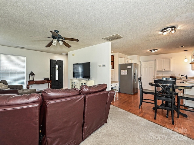 living room with ceiling fan, hardwood / wood-style floors, a textured ceiling, and sink