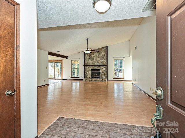 unfurnished living room featuring a stone fireplace, ceiling fan, lofted ceiling, and light wood-type flooring