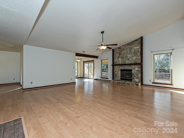 unfurnished living room with plenty of natural light, light hardwood / wood-style floors, a stone fireplace, and lofted ceiling