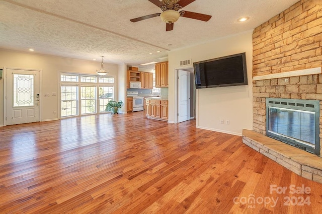 unfurnished living room with a stone fireplace, ceiling fan, a textured ceiling, and light wood-type flooring