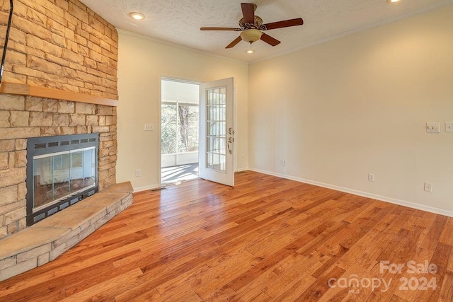 unfurnished living room with a textured ceiling, ceiling fan, crown molding, light hardwood / wood-style floors, and a stone fireplace