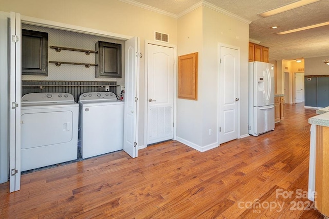 laundry room featuring cabinets, a textured ceiling, washer and clothes dryer, crown molding, and hardwood / wood-style flooring