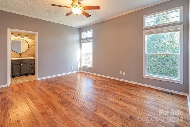 unfurnished bedroom featuring connected bathroom, multiple windows, ceiling fan, and light wood-type flooring