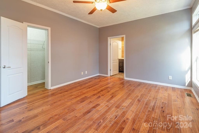 unfurnished bedroom featuring a walk in closet, ceiling fan, light wood-type flooring, a textured ceiling, and a closet