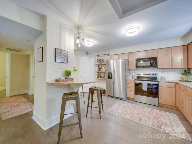 kitchen with decorative light fixtures, light wood-type flooring, stainless steel appliances, and a breakfast bar area