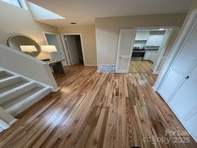 hallway with light wood-type flooring and a skylight