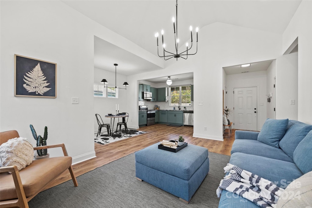 living room featuring sink, high vaulted ceiling, wood-type flooring, and a notable chandelier