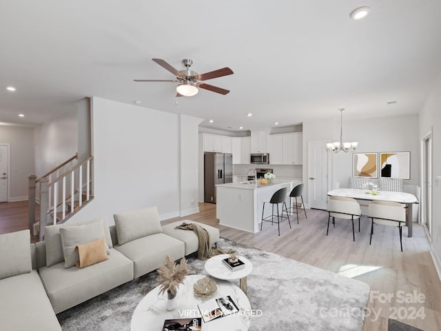 living room with ceiling fan with notable chandelier, light wood-type flooring, and sink