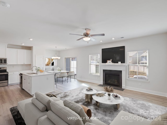 living room featuring ceiling fan with notable chandelier, light hardwood / wood-style floors, and sink