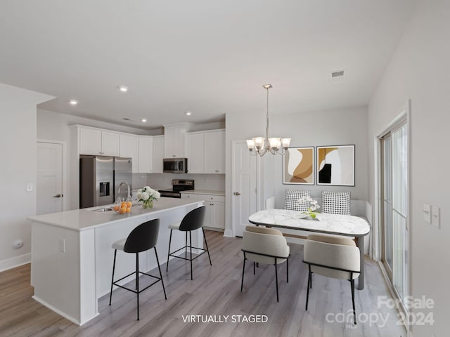 kitchen with a kitchen island with sink, light hardwood / wood-style flooring, white cabinets, and stainless steel appliances