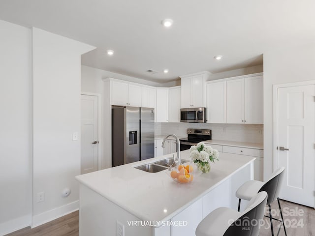 kitchen featuring stainless steel appliances, a kitchen island with sink, sink, white cabinets, and light hardwood / wood-style floors