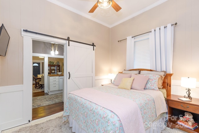 bedroom with a barn door, hardwood / wood-style flooring, ceiling fan, and crown molding