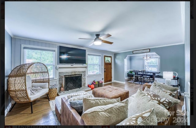 living room featuring a stone fireplace, crown molding, a healthy amount of sunlight, and hardwood / wood-style flooring