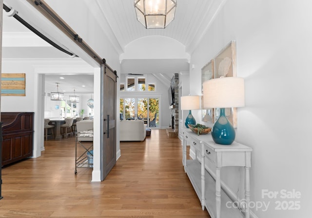 corridor featuring french doors, light hardwood / wood-style flooring, vaulted ceiling, and a barn door