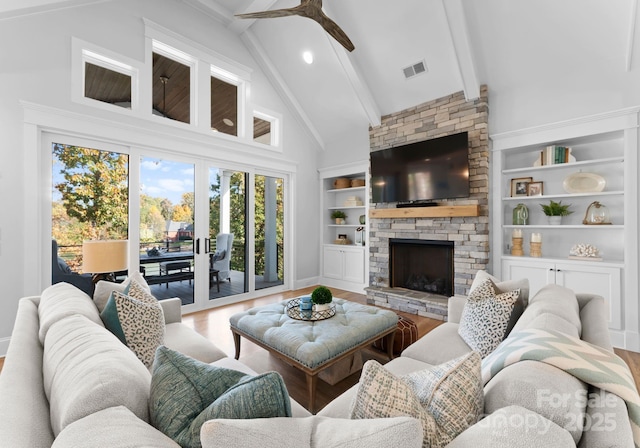 living room featuring ceiling fan, built in shelves, hardwood / wood-style floors, a fireplace, and beamed ceiling