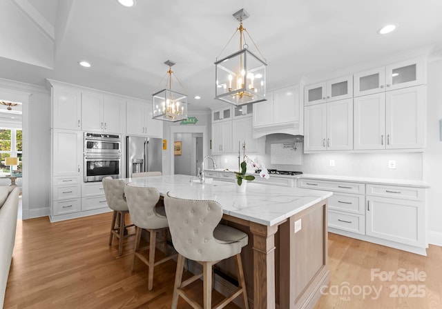 kitchen featuring decorative light fixtures, a kitchen island with sink, white cabinetry, and stainless steel appliances