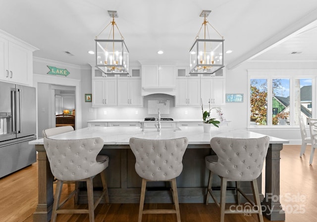 kitchen with white cabinetry, high end fridge, hanging light fixtures, and a spacious island