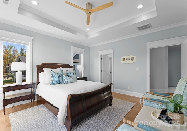 bedroom featuring ceiling fan, crown molding, light hardwood / wood-style floors, and a tray ceiling