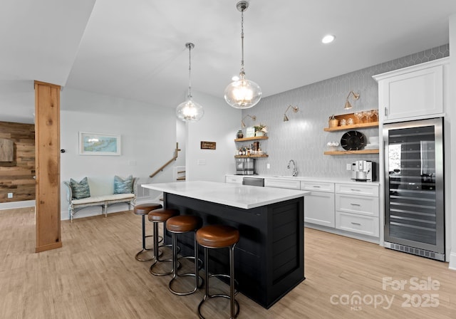 kitchen featuring light hardwood / wood-style flooring, wine cooler, decorative light fixtures, white cabinetry, and a center island