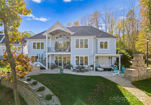 rear view of property with a balcony, a patio area, an outdoor living space with a fireplace, and a lawn