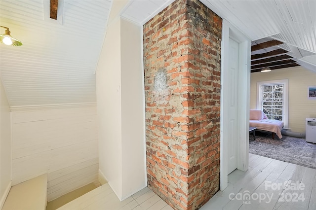 interior space with beam ceiling, light hardwood / wood-style flooring, and brick wall