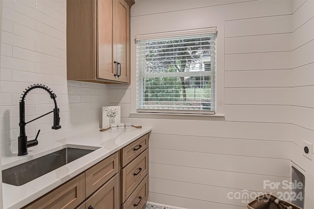 kitchen with backsplash, light stone counters, sink, and wooden walls