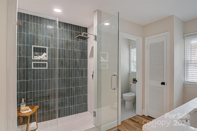 bathroom featuring wood-type flooring, toilet, and a shower with shower door