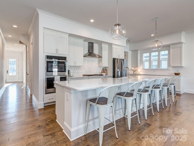 kitchen with wall chimney exhaust hood, hanging light fixtures, stainless steel appliances, and a large island with sink