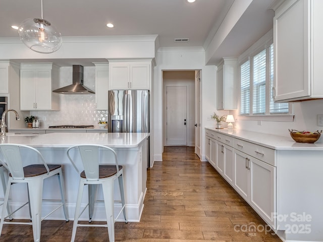 kitchen featuring white cabinetry, sink, stainless steel appliances, wall chimney range hood, and decorative light fixtures