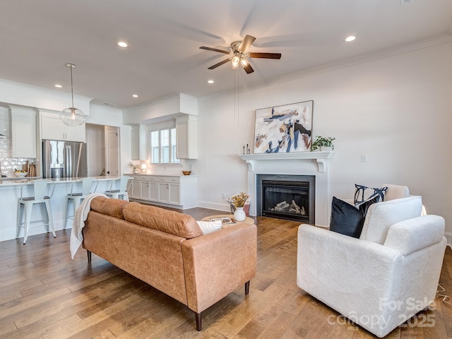 living room featuring light hardwood / wood-style flooring, ceiling fan, and crown molding