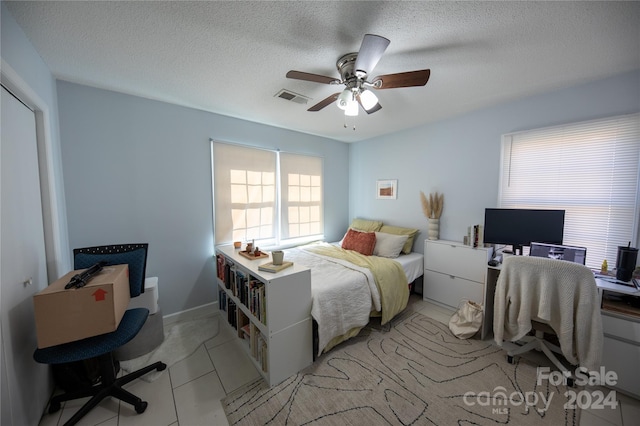 tiled bedroom with ceiling fan and a textured ceiling