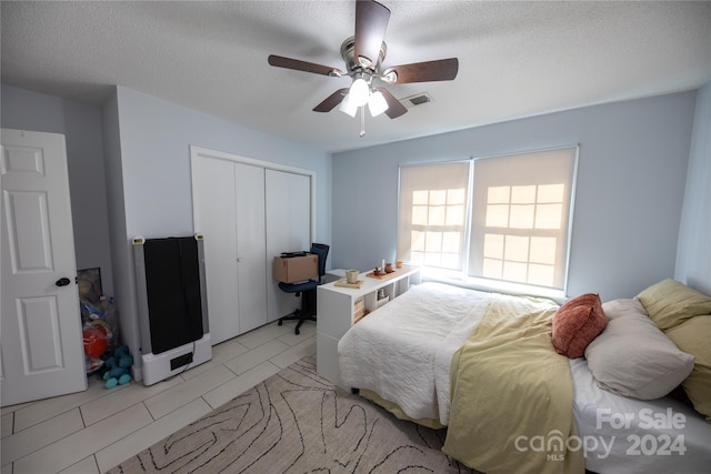 bedroom with ceiling fan, a closet, light tile patterned flooring, and a textured ceiling