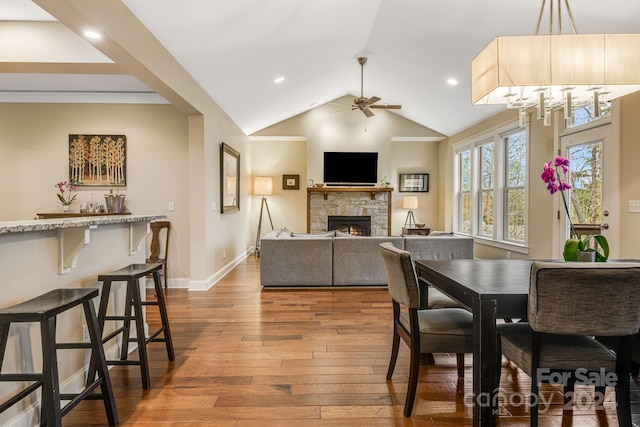 dining area featuring a stone fireplace, vaulted ceiling, hardwood / wood-style flooring, ceiling fan, and ornamental molding