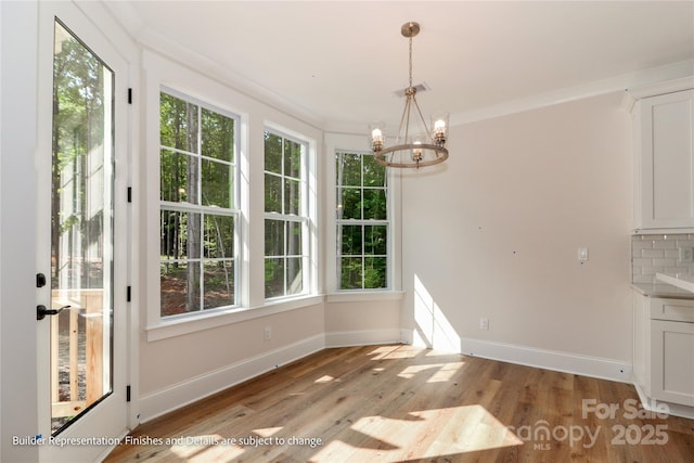unfurnished dining area with light wood-type flooring, baseboards, and an inviting chandelier